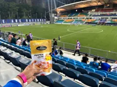 Kemasan Permen Jahe Padjajaran dipegang di tribun sebuah stadion sepak bola